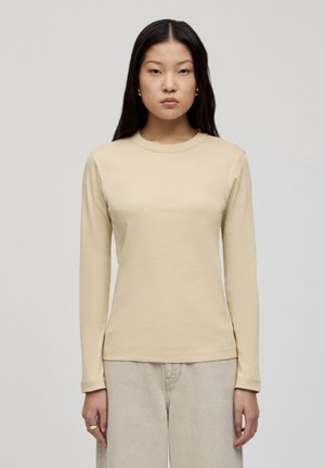 Lange mouwen, ronde hals top in lichtbeige katoen. Heeft een zachte textuur en een aansluitende pasvorm, gedragen met lichte broek.