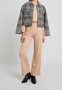 Szara i czarna kurtka w kratę o kroju krótkim, beżowy sweter w prążki oraz szerokie beżowe spodnie. Stylizacja uzupełniona czarnymi botkami na obcasie.
