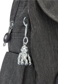 Sac à dos en tissu gris avec une finition texturée, doté d'un charme en métal représentant un singe argenté fixé à une boucle, et de deux tirettes de fermeture éclair.