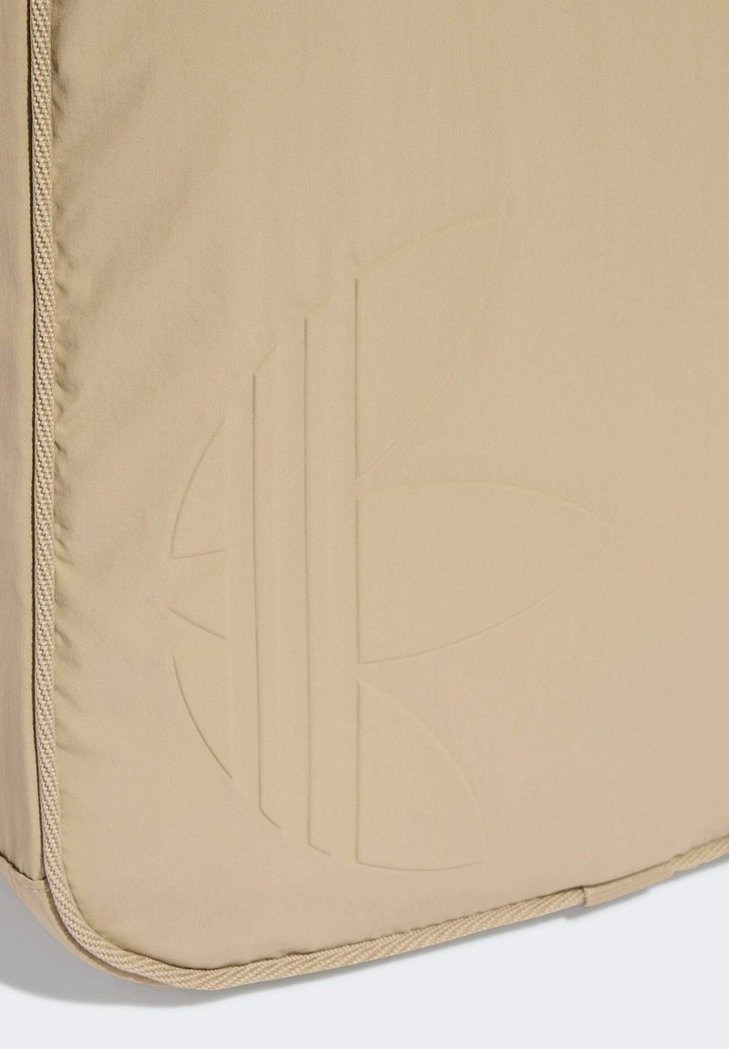 Superficie in tessuto beige con logo a rilievo a tre petali e cuciture bordate a tubolare sui lati sinistro e inferiore.