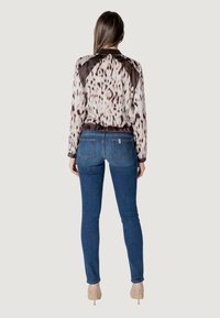 Blusa a maniche lunghe con una leggera stampa animale e dettagli scuri sulle spalle, abbinata a jeans blu aderenti e décolleté color nude.