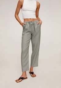 Lichtgroene, getextureerde, elastische broek met zakken. Gecombineerd met een witte geribbelde crop top en zwarte platte sandalen. Eenvoudig, ontspannen ontwerp.