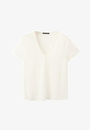 T-shirt blanc à manches courtes avec col en V, coupe légèrement ample et petite étiquette noire à l'intérieur du col.