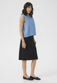 Blue denim sleeveless top with a round neckline, paired with a fitted black knee-length skirt and black flat shoes with a bow accent.