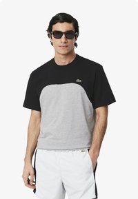 Camiseta bloqueada en negro y gris de manga corta y cuello redondo. Presenta un logo bordado en verde en el pecho.