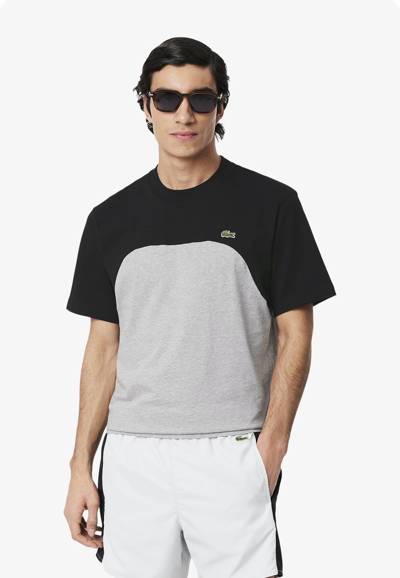 Camiseta bloqueada en negro y gris de manga corta y cuello redondo. Presenta un logo bordado en verde en el pecho.