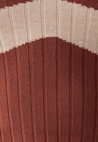 Maglione lavorato a maglia con texture a coste in tonalità alternate di ruggine e beige, dotato di un motivo di design curvo sulla parte anteriore.