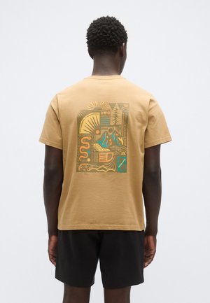 Rjava bombažna majica s kratkimi rokavi, na hrbtni strani je grafični dizajn z abstraktnimi elementi v rumeni, zeleni in modri barvi.