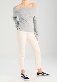 Pull gris à épaules dénudées avec texture côtelée, associé à un jean blanc raccourci et des baskets noires avec des lacets blancs.