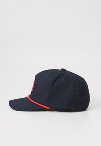 Casquette marine avec accent rouge sur la visière, pic incurvé et logo brodé à l'avant. Texture lisse et forme structurée. Vue arrière montrée.