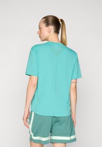 Camiseta turquesa de manga corta, con escote redondo y un detalle de malla en forma de diamante en la espalda, combinada con pantalones cortos verdes con rayas blancas.