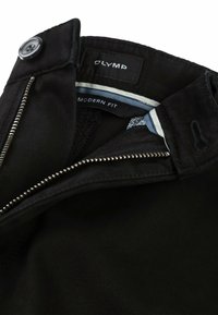 Zwarte broeken met een ritssluiting en knoopsluiting. Het label aan de binnenkant leest "OLYMP MODERN FIT." De stof heeft een gladde textuur en een subtiele glans.