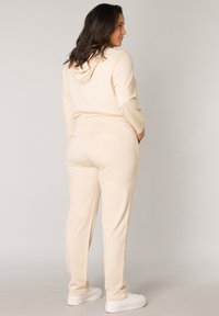 Beige hoodie en bijpassende broekset, gemaakt van zachte stof, met een capuchon, lange mouwen en zijzakken. Draagt met witte sneakers.