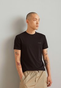 T-shirt nera in cotone con maniche corte, caratterizzata da un piccolo logo ricamato sul petto, abbinata a pantaloni corti beige chiaro.
