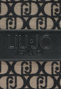Liu Jo Milano Tasche aus einem schwarzen und beigen gemusterten Canvas mit einem schwarzen strukturierten Leder-Logopatch. Auffällige runde und Buchstabenmuster.