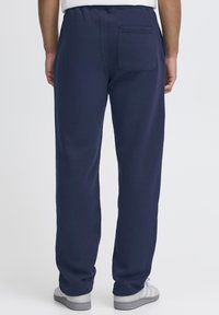 Temno modre trenirke s prilegajočim elastičnim pasom, z enim zadnjim žepom in ohlapnim krojem z ravnimi nogavicami. Lahka tekstura tkanine.