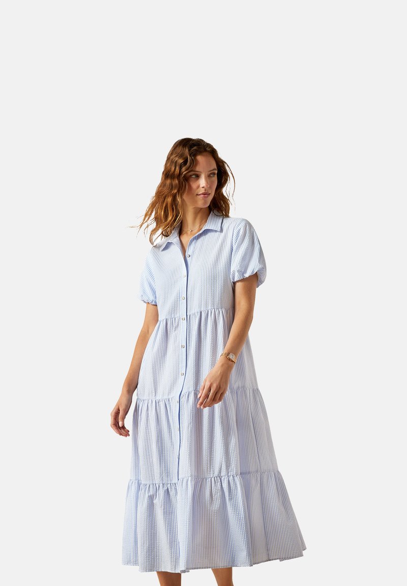 Gestreiftes Kleid in Blau und Weiß mit Knopfverschluss, kurzen Puffärmeln, mehreren Rüschenschichten am Saum und lockerer Passform. Hergestellt aus leichtem Stoff.