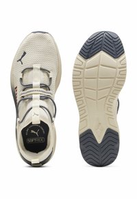 Zapatillas deportivas beige con parte superior de malla, cordones elásticos y una suela acolchada que presenta una suela exterior de goma negra texturizada y detalles de logotipo.