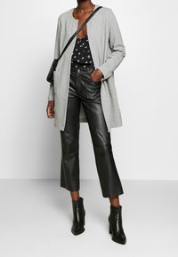 Šedý pletený kardigan s volnějším střihem a otevřeným předním dílem, doplněný o vysoké černé kožené kalhoty a černé kotníkové boty na podpatku.