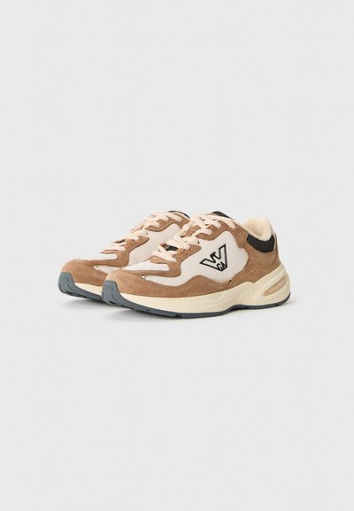 Et par beige og brune ruskind sneakers med mesh-paneler, snørebånd og en sort logo på siderne, præsenteret på en ensfarvet baggrund.