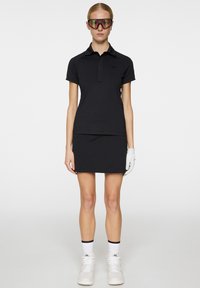 Czarny polo z kołnierzykiem, zestawiony z czarną spódnicą. Dodatki to dużych rozmiarów kolorowe okulary przeciwsłoneczne i białe buty sportowe.