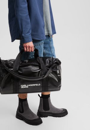 Black duffel bag with logo, durable material, and top handles. Gray suede ankle boots with black rubber soles and elastic side panels.