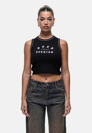 Top corto nero con testo bianco "GOOD for NOTHING" in diversi caratteri, abbinato a jeans in denim scuro con vita alta. Texture liscia.