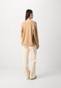 Beige ullgenser med løs passform, kombinert med kremfargede vidbenede bukser. Jevn tekstur og minimalistisk design, vist fra en bakvinkel.