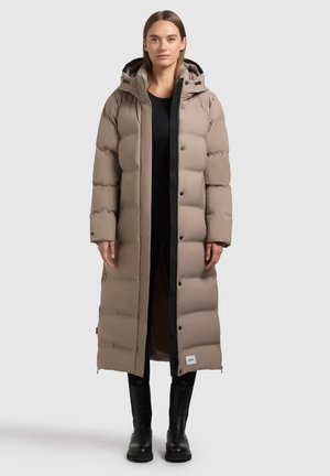 Manteau long et rembourré beige avec une fermeture éclair noire et des accents noirs. Il dispose d'une capuche, de boutons-pression, et est fabriqué dans un tissu lisse et matelassé.