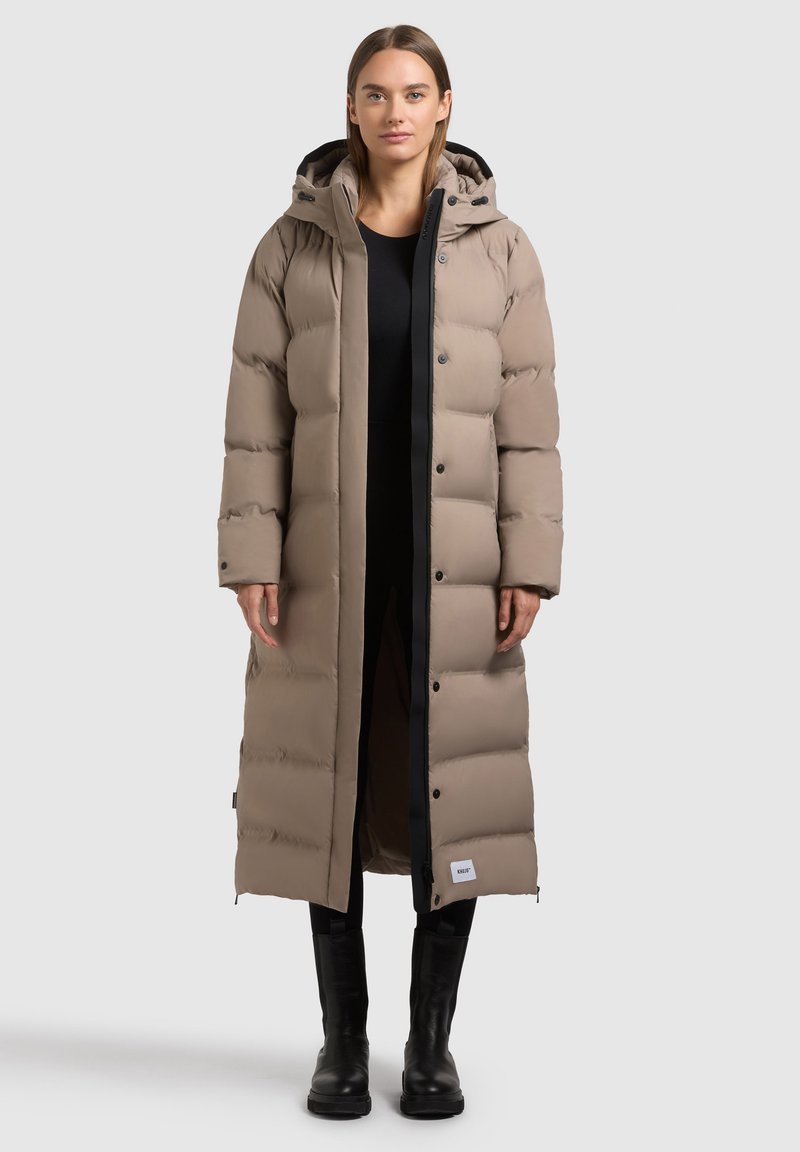 Lange, gevoerde jas in beige met een zwarte rits en accenten. Heeft een capuchon, drukknoopsluiting en is gemaakt van een gladde, gequiltte stof.