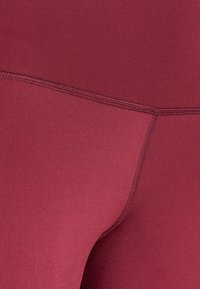 Leggings bordeaux realizzati in tessuto elastico, con cuciture piatte e una superficie liscia per il comfort e la libertà di movimento.