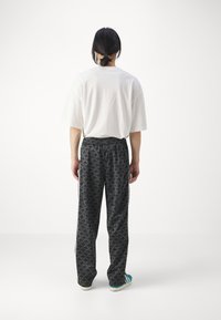 Vit oversized t-shirt, svarta mönstrade byxor med blommönster och teal-färgade sneakers med accent. Avslappnad passform med elastisk midja.