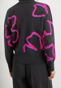Svart tröja med rosa och lila abstrakta vågiga mönster, stickad textur och rund halsringning. Designen täcker baksidan och ärmarna.