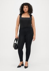 Μαύρο κορμάκι με τετράγωνη λαιμόκοψη, συνδυασμένο με μαύρες κολάν και μια μικρή τσάντα. Λείο υλικό; εφαρμοστή σιλουέτα; μινιμαλιστικός σχεδιασμός.