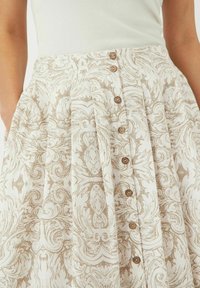 Beige mønstret skjørt med et flytende design og folder, samt fem treknapper foran. Laget av lett stoff.