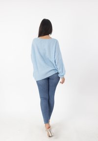 Suéter de punto de gran tamaño en azul claro con un patrón texturizado, combinado con jeans ajustados en azul oscuro y sandalias de tacón cuadrado plateadas.