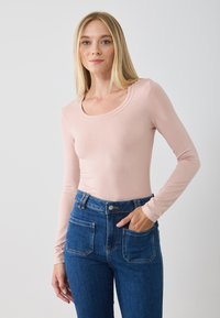 Helles rosa Langarmshirt mit Rundhalsausschnitt, kombiniert mit hochgeschnittenen blauen Jeans aus Denim mit vorderen Taschen und Stickdetails.