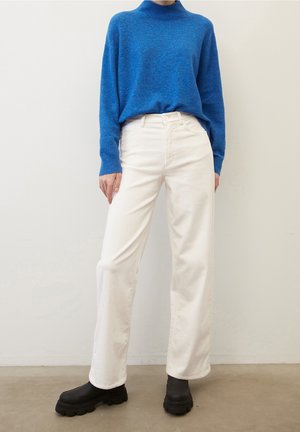 Suéter de cuello alto tejido azul, pantalones anchos blancos y botines negros gruesos. Texturas suaves con diseños lisos y sin patrones.