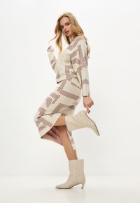 Set de pulover și fustă tricotat în crem, cu un model geometric burgund, completat de botoși bej cu vârf ascuțit și toc kitten.