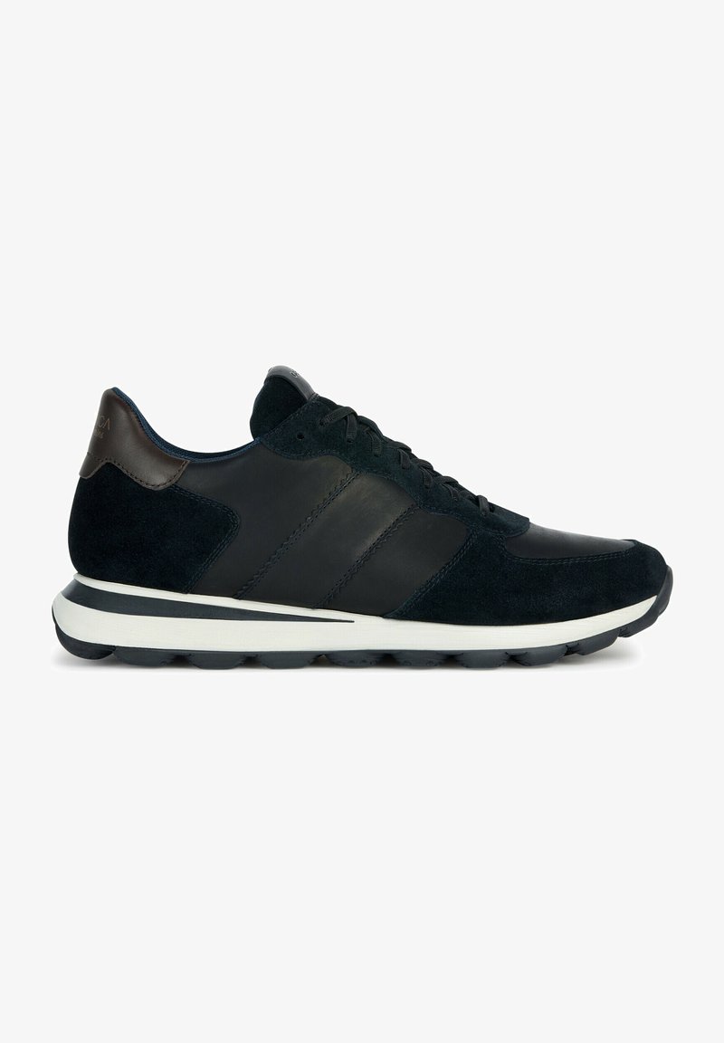 Zapatillas deportivas negras de ante y cuero, con diseño de tres rayas, suela blanca y un acento de cuero marrón en el talón.