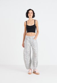 Wijde broek met een bloemmotief in grijs, gemaakt van een lichtgewicht stof. Gepaarde met een zwart tanktop en roze sneakers.