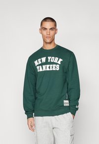 Grønn hettegenser med "NEW YORK YANKEES" trykket med fete hvite bokstaver på forsiden. Har rund hals og ribbestrikkede mansjetter.
