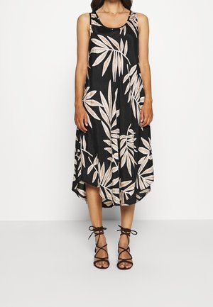 Schwarzes ärmelloses Midikleid mit beigem tropischem Blattmuster, kombiniert mit schwarzen Schnürsandalen mit hohem Absatz.