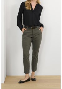 Blouse noire à manches longues, pantalon vert olive ajusté avec une ceinture, et ballerines noires avec un détail en nœud. Design simple et ajusté.
