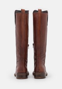 Botas de cuero marrón hasta la rodilla con un acabado suave, cremalleras laterales y lengüetas en la parte superior. Suelas marrones resistentes.