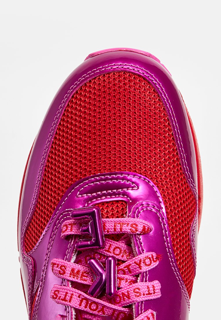 Baskets rouges vives avec une tige en mesh, des accents roses brillants, une semelle en caoutchouc proéminente et des lacets à motifs avec du texte.