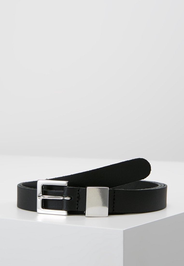 Ceinture en cuir noir avec une boucle rectangulaire argentée et une boucle carrée argentée reposant sur une surface blanche.