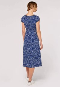 Blå klänning med ett blommigt, vitt abstrakt mönster. Kappärmar, smockad midja och mittlång fåll. Kombinerad med vita sneakers.