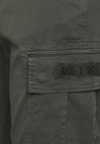 Temnozeleni cargo hlače imajo na stranski žepu fabric patch z označbo "MILJ 820", vidno šivanje in trpežno teksturo.