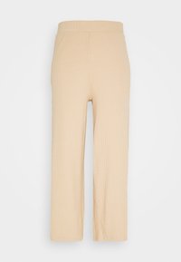Pantalons beige à côtes avec une coupe évasée et une taille élastique. Le matériau semble doux avec une texture subtile et sans fermetures visibles.